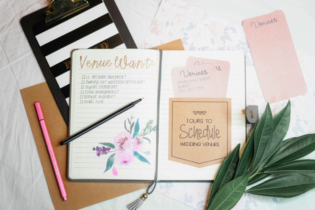 Flat-lay photo of a wedding planner, checklist with scribbles, and colorful pens on a pastel background.